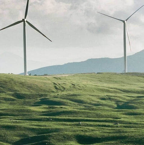 Image of wind turbines on a green hill with a blue cloudy sky