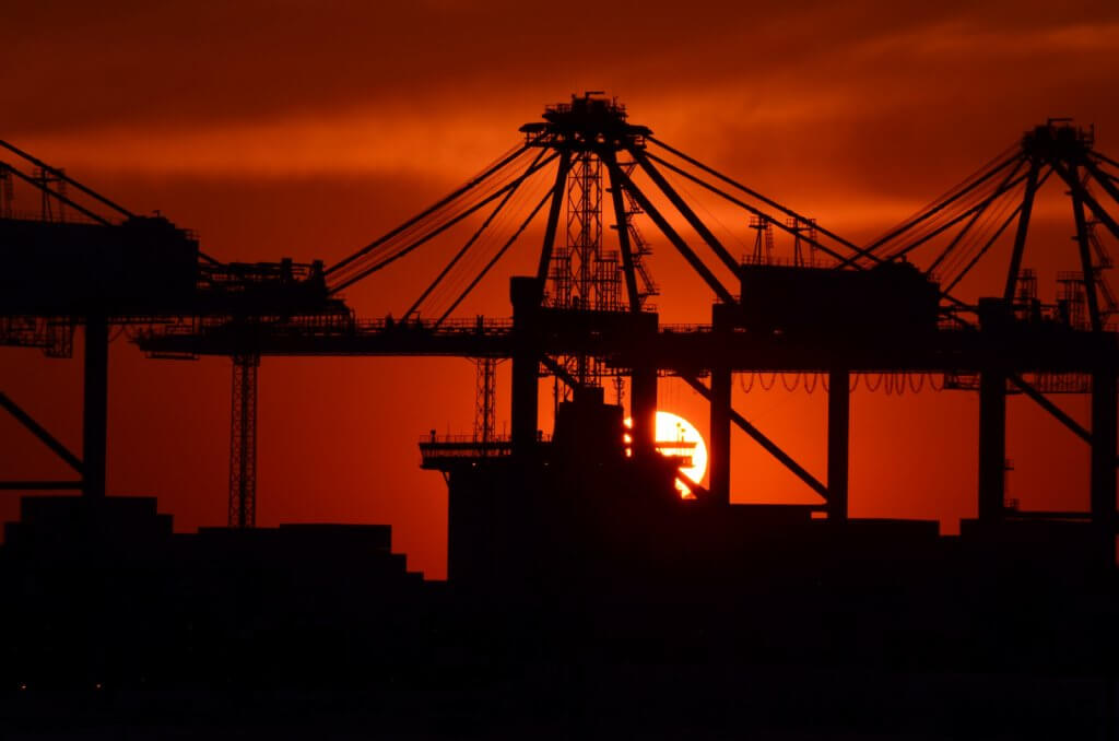 Image of a port at sunset with large crane silhouettes